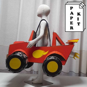 May include: A red cardboard monster truck with yellow wheels and a yellow flame design. The truck is being held by a person wearing a white shirt.
