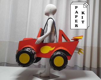 May include: A red cardboard monster truck with yellow wheels and a yellow flame design. The truck is being held by a person wearing a white shirt.