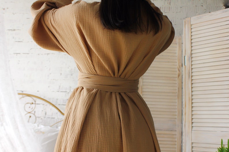 May include: A long, brown, loose-fitting dress with a self-tie belt. The dress is made of a soft, textured fabric.