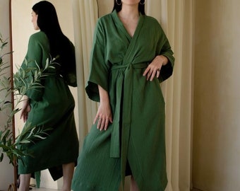 May include: A woman wearing a green, long-sleeved, wrap-style robe with a matching sash. She is standing in front of a mirror and has her hair pulled back.