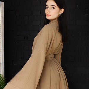 May include: A woman wearing a long, brown robe with wide sleeves. The robe is made of a soft, textured fabric and has a belt at the waist.