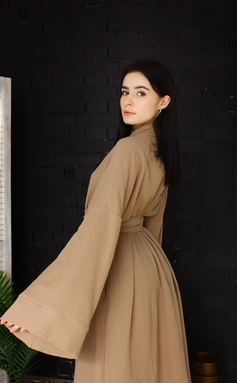 May include: A woman wearing a long, brown robe with wide sleeves. The robe is made of a soft, textured fabric and has a belt at the waist.