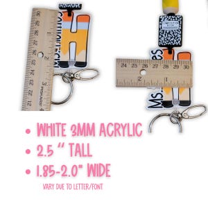 May include: White acrylic keychain with the text "MS." and a pencil design. The keychain is 2.5 inches tall and 1.85-2.0 inches wide. Includes a silver-colored clasp for attaching to keys or a bag.