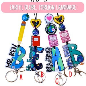 May include: A collection of teacher-themed lanyards with globe and school-related charms. Each lanyard features a large letter spelling out a name, such as "BEN" and "BEAB", with a keyring attached. The lanyards have a variety of charms, including pencils, hearts, and books.