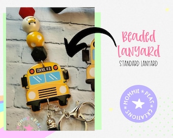 Puede incluir: Un cordón de cuentas con un dije de autobús escolar amarillo. El cordón presenta una mezcla de cuentas rojas, blancas, amarillas y negras. El dije tiene las palabras "SCHOOL BUS". También se ve el texto "Beaded Lanyard Standard Lanyard".