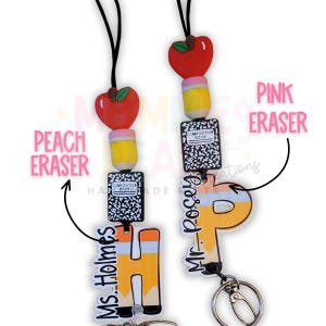 May include: Two lanyards with school-themed charms. Each lanyard features a red apple, a yellow pencil, and a composition book charm. One lanyard has a pencil charm with the name "Ms. Holmes" and a pencil-shaped charm. The other has a pencil charm with the name "Mr. Posey" and a pencil-shaped charm.