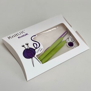 May include: A white packaging with the text "KnitUK" and a picture of two green and purple crochet hooks. The packaging is shaped like a pillow.