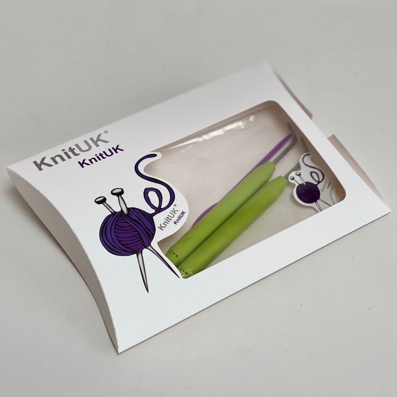 May include: A white packaging with the text "KnitUK" and a picture of two green and purple crochet hooks. The packaging is shaped like a pillow.