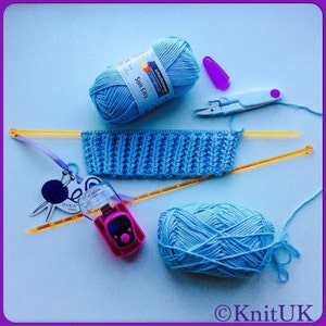 May include: A blue knitting project with two balls of yarn, knitting needles, a stitch counter, and a pair of scissors. The yarn is labeled "Schachenmayr - Original Sun City".