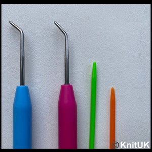 K&ouml;nnte beinhalten: Vier H&auml;kelnadeln, zwei mit blauen, rosa und gr&uuml;nen Griffen und zwei mit gr&uuml;nen und orangen Griffen. Die H&auml;kelnadeln sind aus Metall und haben eine gebogene Spitze.