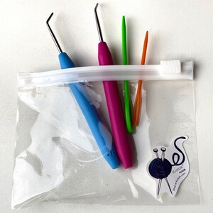 K&ouml;nnte beinhalten: Eine transparente Plastikt&uuml;te mit Rei&szlig;verschluss enth&auml;lt vier bunte H&auml;kelnadeln. Die Nadeln sind blau, rosa, gr&uuml;n und orange. Ein kleiner Aufkleber mit dem Text "KnitUK" befindet sich auf der T&uuml;te.