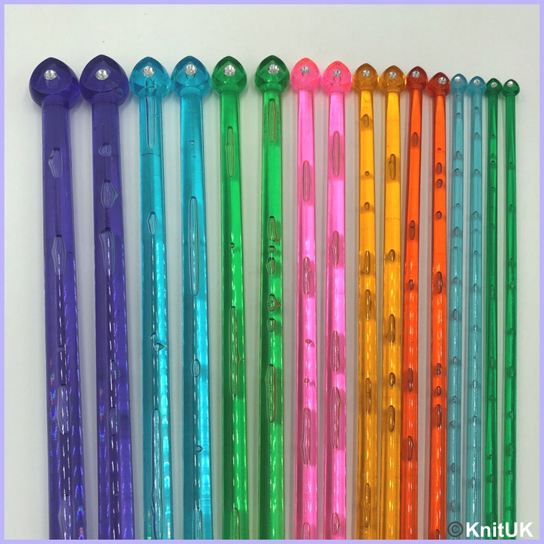 May include: A set of 16 colorful plastic knitting needles with a heart-shaped tip and a clear, textured finish. The needles are arranged in order of size, with the smallest needle on the left and the largest needle on the right.
