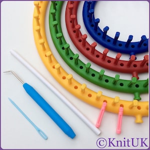 May include: A set of five colourful circular knitting looms in yellow, green, red, blue, and purple. The looms are arranged in a semi-circle with the largest loom at the top. The set also includes two pink and yellow knitting needles, a blue crochet hook, and a white knitting needle.