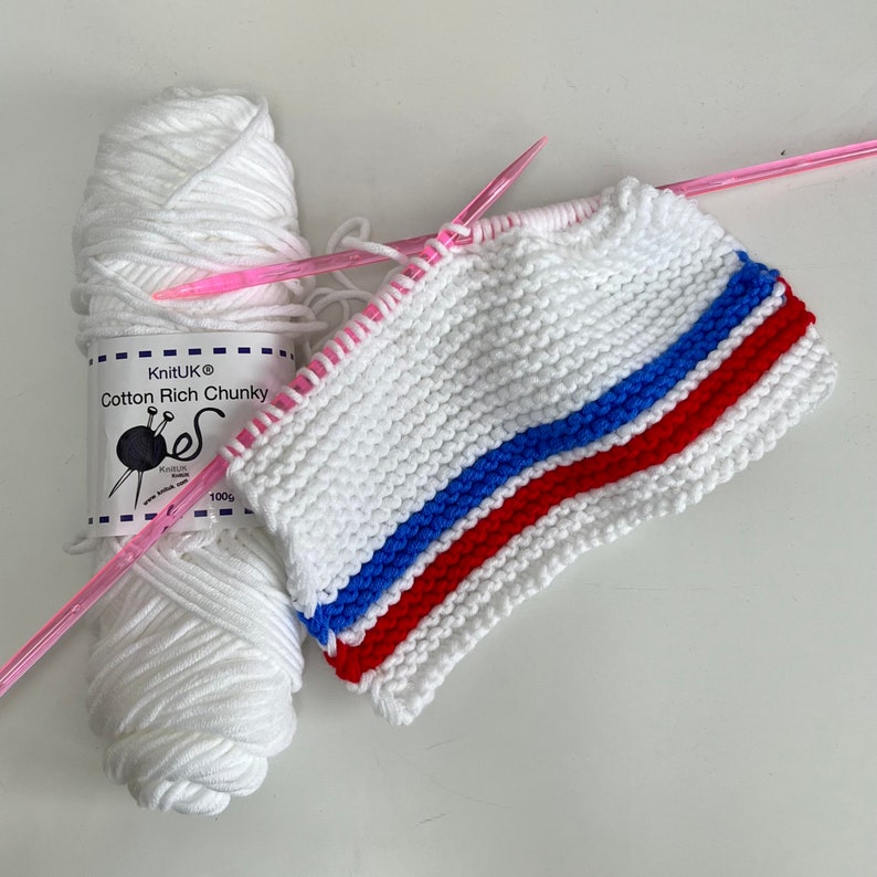 May include: White yarn with a red, blue, and white striped knitted fabric. The yarn label reads "KnitUK Cotton Rich Chunky 100g".