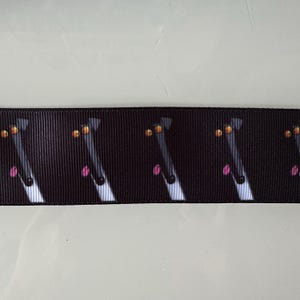 May include: Black and white ribbon with a repeating pattern of dog faces. The dogs have black noses, pink tongues, and orange eyes.