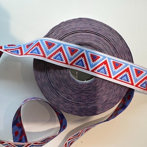 May include: A roll of purple ribbon with a geometric pattern in red, white, and blue. The ribbon features a repeating design of triangles and zigzags. The ribbon is likely used for crafting or decorative purposes.