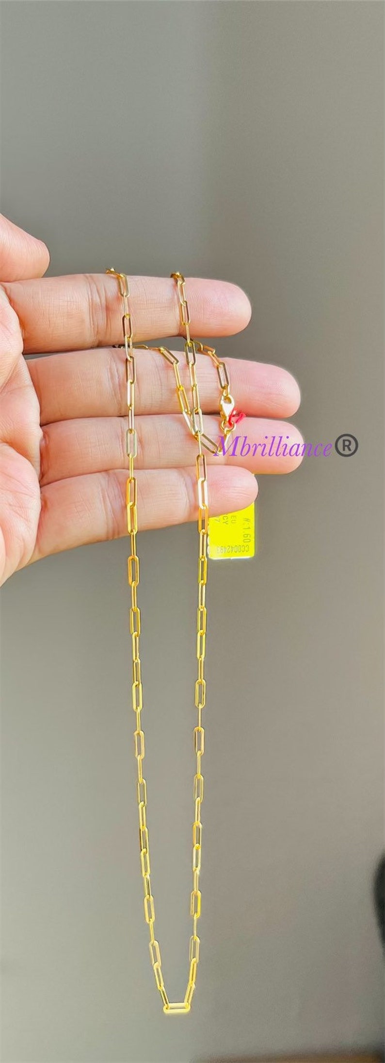 Puede incluir: Un collar de cadena de oro con una etiqueta de papel que dice "#5160 50 2CY". La etiqueta tambi&eacute;n tiene el texto "Mbrilliance" y un s&iacute;mbolo de marca registrada.