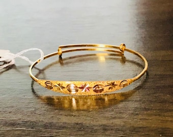 May include: A gold-colored adjustable bracelet with a decorative central band. The band features a textured surface with star and oval-shaped cutouts. The bracelet is designed to be adjustable for a comfortable fit.