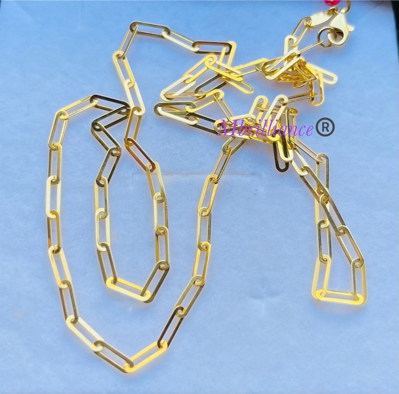 Puede incluir: Un collar de cadena de oro con un dise&ntilde;o delicado y enlazado. La cadena est&aacute; hecha de peque&ntilde;os eslabones rectangulares que est&aacute;n conectados entre s&iacute; para formar un bucle continuo. La cadena se muestra sobre un fondo blanco.