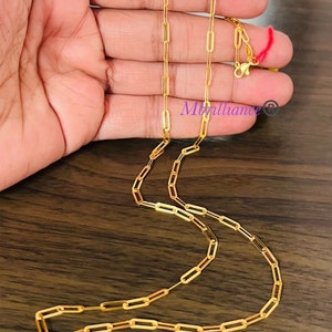 Puede incluir: Un collar de cadena de oro con un estilo de cadena de clip de papel. La cadena est&aacute; sobre una superficie de madera.