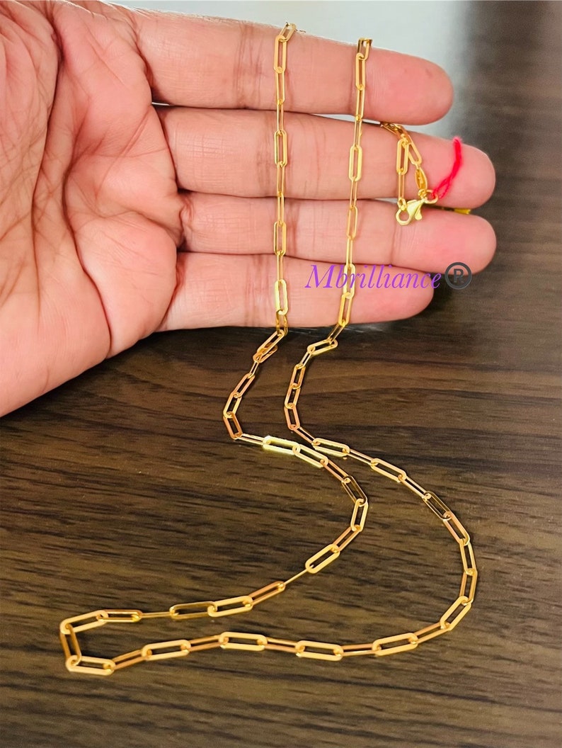 Puede incluir: Un collar de cadena de oro con un estilo de cadena de clip de papel. La cadena est&aacute; sobre una superficie de madera.