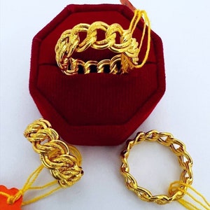 May include: Three gold-colored chain link rings. One ring is displayed inside a red velvet ring box. The other two rings are on a white surface. Each ring has a yellow tag attached.