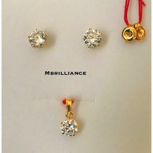 May include: A jewelry set featuring a pair of stud earrings and a pendant, all with a gold setting and a large, clear, faceted stone. The earrings and pendant are displayed on a white background. The text "MBRILLIANCE" is printed in the center.