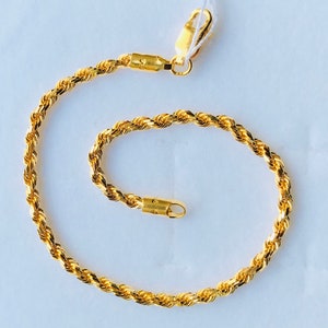 Könnte beinhalten: Ein goldfarbenes Armband mit Seilkette und Karabinerverschluss. Das Armband besteht aus verdrehten Metallgliedern, wodurch eine seilartige Textur entsteht. Der Verschluss und die Verbindungselemente sind ebenfalls goldfarben.