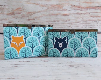 May include: Two turquoise fabric coin purses with a woodland animal print. The larger purse features a fox and the smaller purse features a bear. Both purses have a silver metal frame.