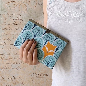 May include: A teal blue and orange fabric purse with a fox design. The purse has a metal clasp and a leafy pattern.