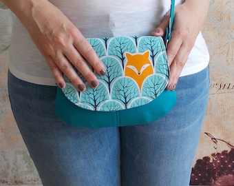 May include: A teal blue crossbody bag with a flap closure. The flap features a repeating pattern of blue trees and a bright orange fox face.