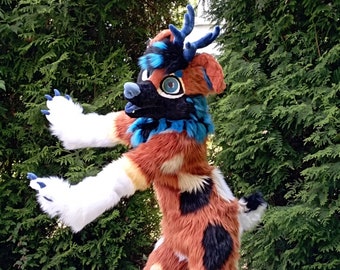 May include: A furry orange, black, and white deer-like costume with blue accents and antlers. The costume is standing on a black and white tiled floor.