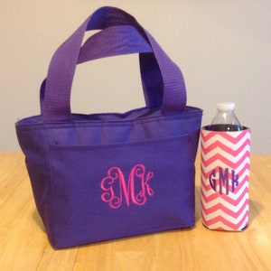 K&ouml;nnte beinhalten: Lilafarbene isolierte Lunch-Tasche mit einem Monogramm-Design und einem Getr&auml;nkehalter mit pink-wei&szlig;em Chevron-Muster.