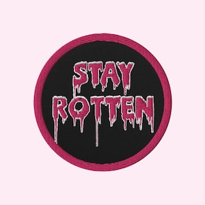 Può includere: Toppa ricamata con la scritta "STAY ROTTEN" in lettere rosa gocciolanti su sfondo circolare nero. La toppa ha un bordo rosa ed è posta su uno sfondo rosa chiaro. Ideale per personalizzare abbigliamento o accessori.