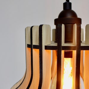 May include: A wooden pendant light with a geometric design. The light is made of thin strips of wood that are arranged in a grid pattern. The light is illuminated by a single light bulb.