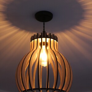 May include: A wooden pendant light fixture with a round, cage-like design. The light is on and illuminates the room with a warm glow.