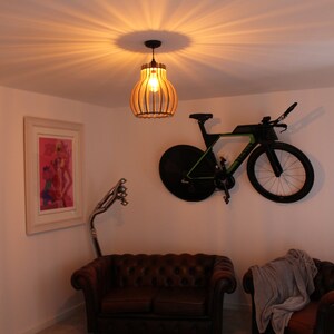 May include: A brown leather sofa and a brown armchair with a gray throw blanket are in a living room with a bicycle hanging on the wall. A wooden pendant light hangs from the ceiling above the sofa.