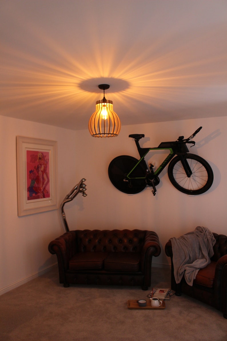May include: A brown leather sofa and a brown armchair with a gray throw blanket are in a living room with a bicycle hanging on the wall. A wooden pendant light hangs from the ceiling above the sofa.