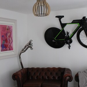 May include: A brown leather chesterfield sofa with a wooden frame and button tufting. A black and green bicycle is mounted on the wall above the sofa. A wooden lampshade with a caged light bulb hangs from the ceiling.