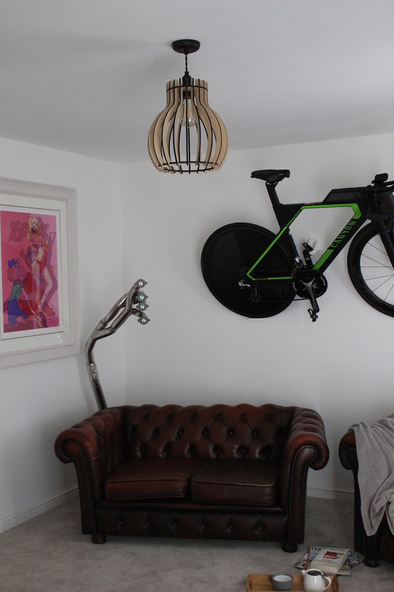 May include: A brown leather chesterfield sofa with a wooden frame and button tufting. A black and green bicycle is mounted on the wall above the sofa. A wooden lampshade with a caged light bulb hangs from the ceiling.