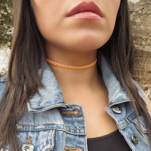 Puede incluir: Un collar gargantilla de cuero marr&oacute;n con tachuelas plateadas. El collar es delgado y tiene un dise&ntilde;o simple.