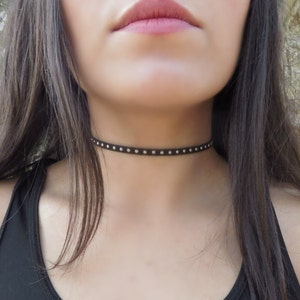 Puede incluir: Un collar gargantilla negro con tachuelas plateadas.