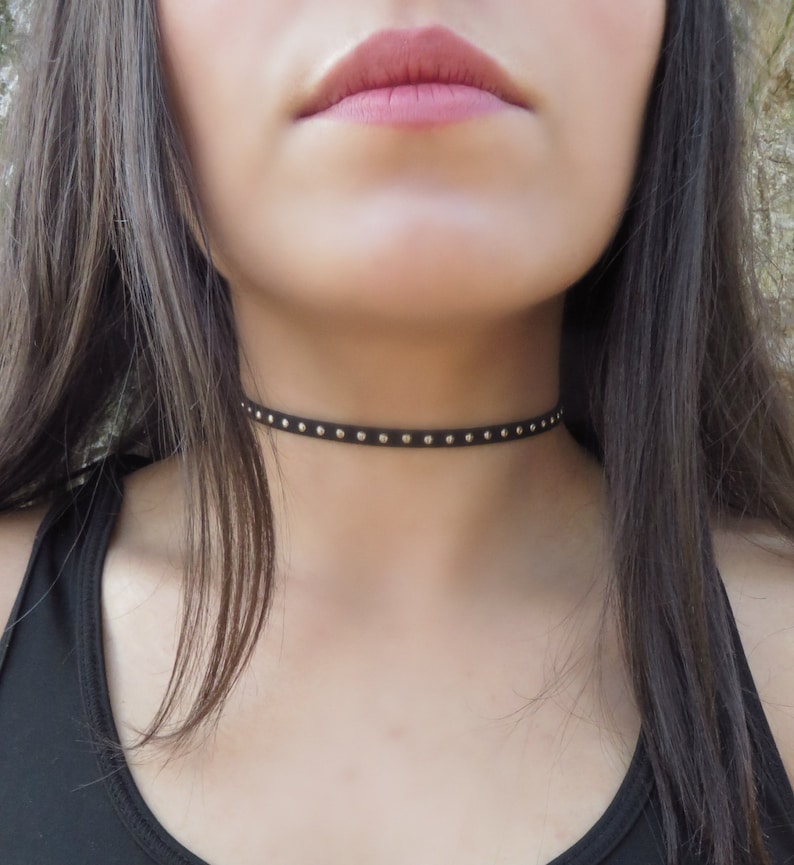 Puede incluir: Un collar gargantilla negro con tachuelas plateadas.
