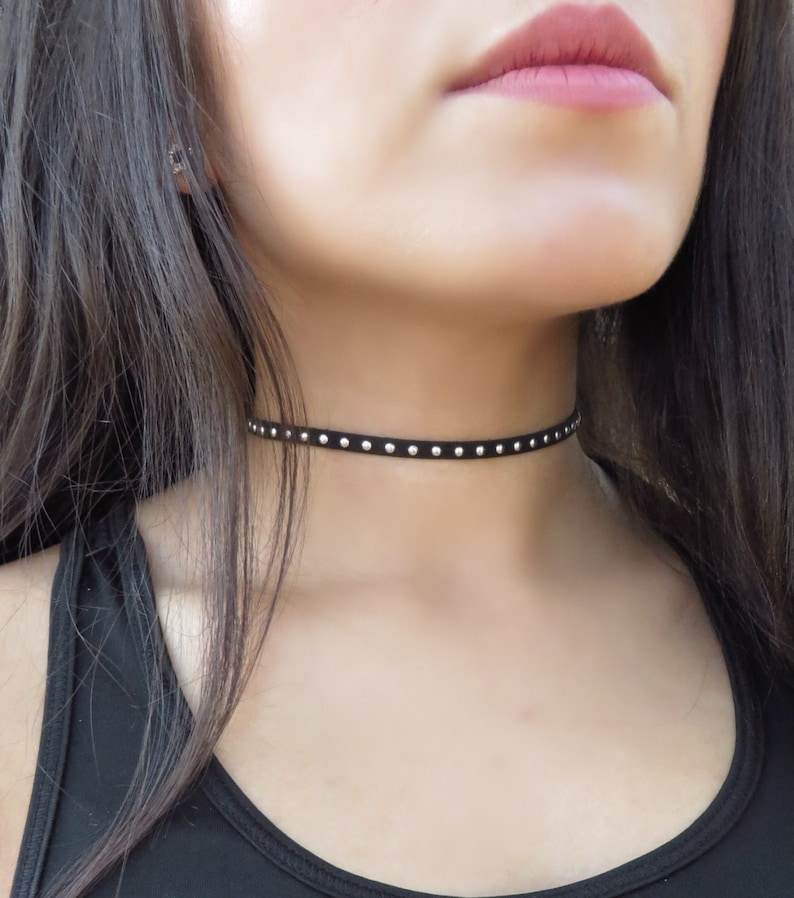 Puede incluir: Un collar gargantilla negro con tachuelas plateadas.