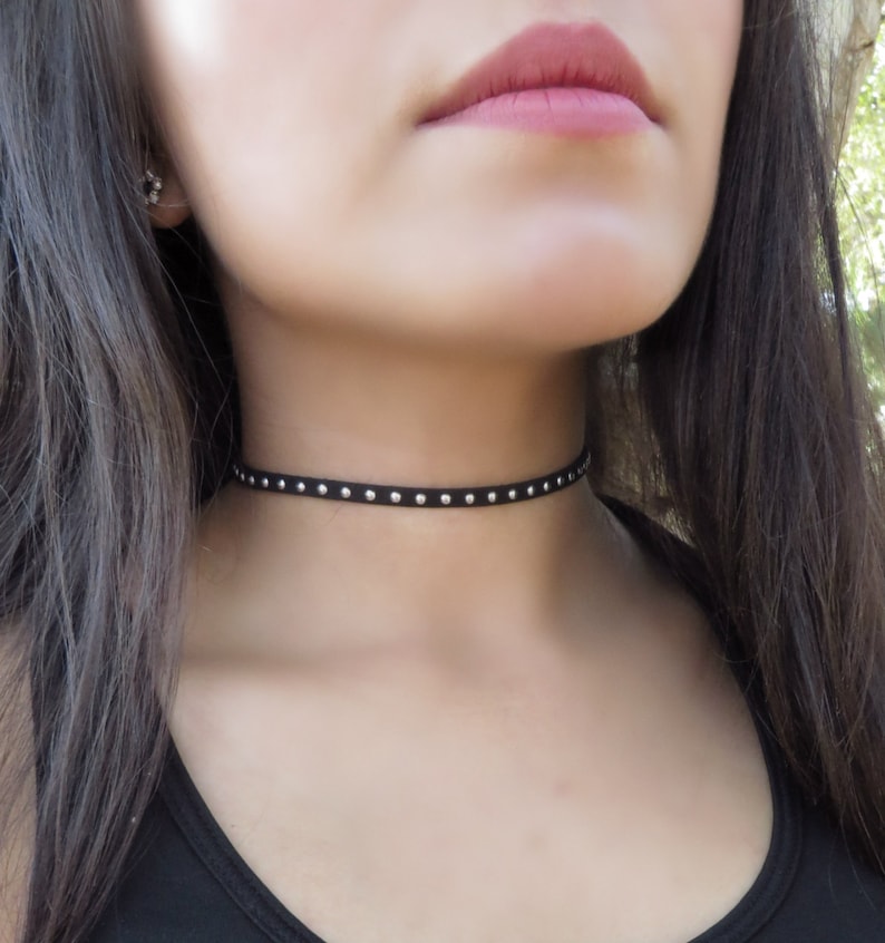 Puede incluir: Un collar gargantilla negro con tachuelas plateadas. La gargantilla est&aacute; hecha de un material fino y suave y es ajustable.