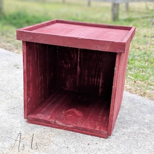 Peut inclure: Une bo&icirc;te en bois rouge avec un dessus carr&eacute; et des c&ocirc;t&eacute;s ouverts. La bo&icirc;te est faite de bois brut et a un aspect rustique.