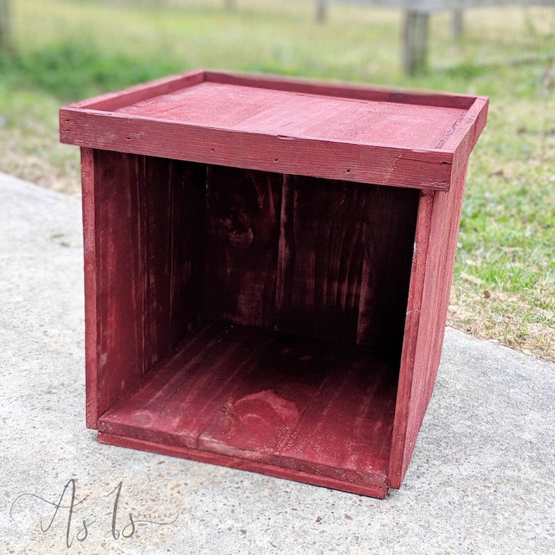 Peut inclure: Une bo&icirc;te en bois rouge avec un dessus carr&eacute; et des c&ocirc;t&eacute;s ouverts. La bo&icirc;te est faite de bois brut et a un aspect rustique.