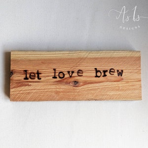 May include: A wooden sign with the text "let love brew" burned into the surface.