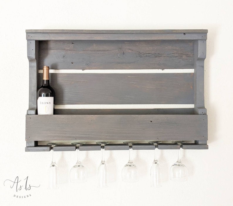 May include: A gray wooden wall-mounted wine rack with a shelf for bottles and a row of glass holders underneath. A bottle of wine labeled "IRONY" is on the shelf.