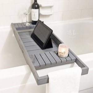 May include: Gray wooden bath tray with a tablet, a candle, and a towel. The candle has the word "namaste" on it.